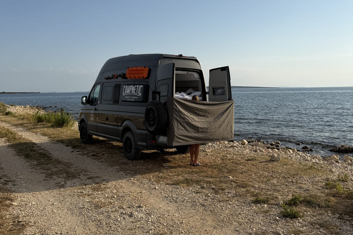 Campnetic-Van am Meer, zwischen den geöffneten Hecktüren hängt ein Sichtschutz zum Duschen