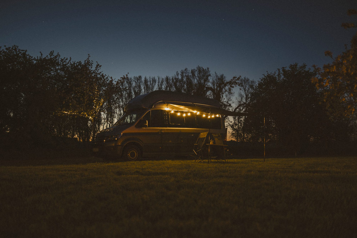 Camper am Abend mit leuchtender Lichterkette unter der ausgefahrenen Markise